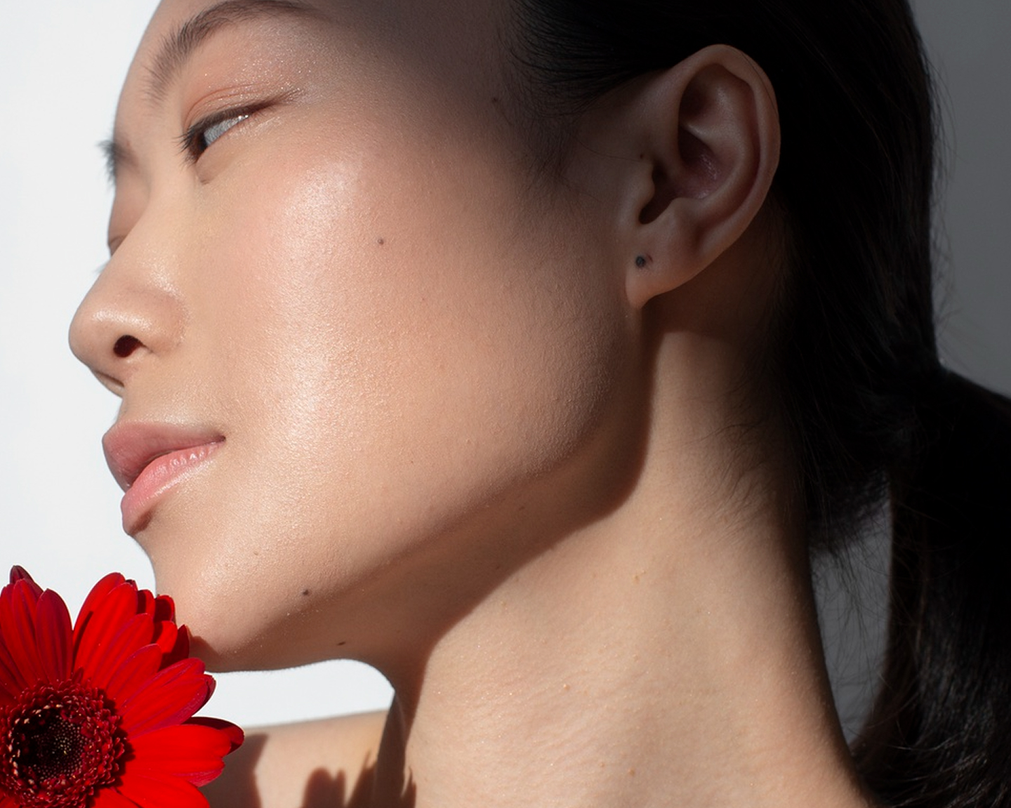 Woman in profile with smooth, even skin holding a red gerbera flower